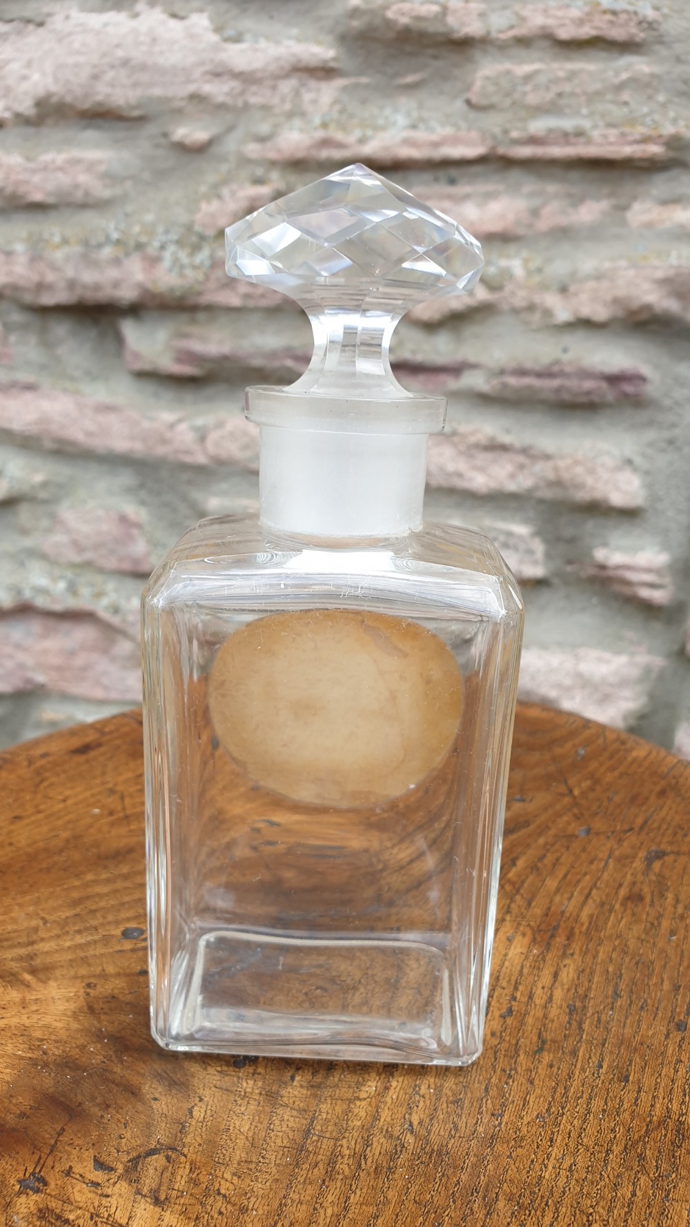 A clear glass rectangular perfume bottle with a faceted geometric stopper and an original circular paper label reading Potter and Moores Mitcham Lavender. View VI