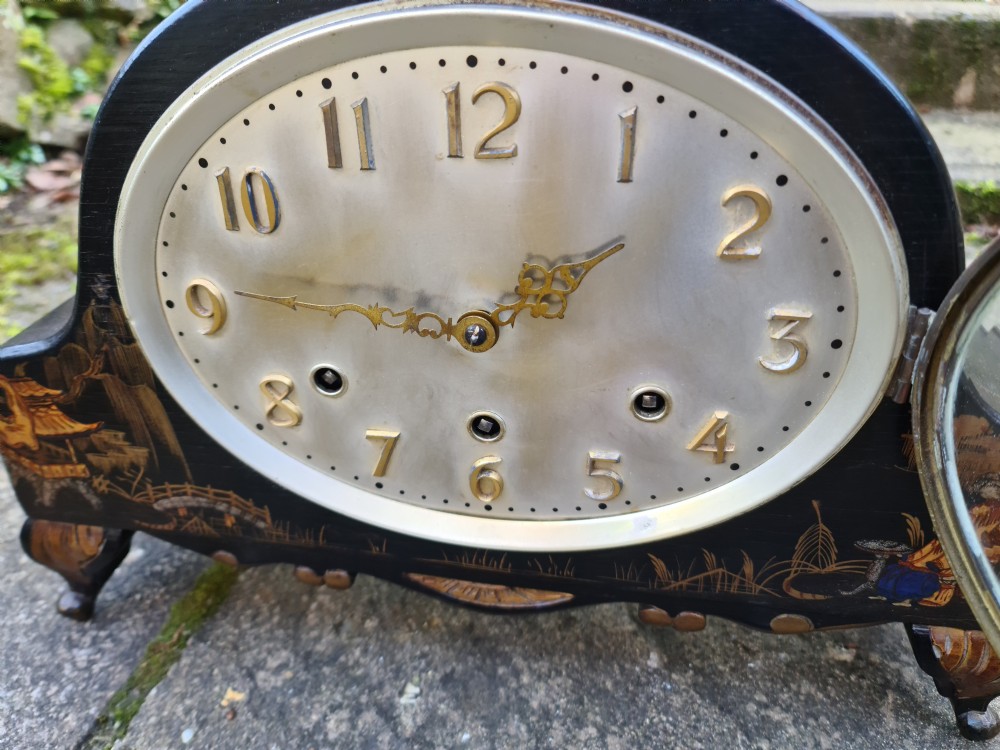 An antique black lacquered mantel clock decorated with gold chinoiserie scenes and an oval brass-rimmed clock face. View V