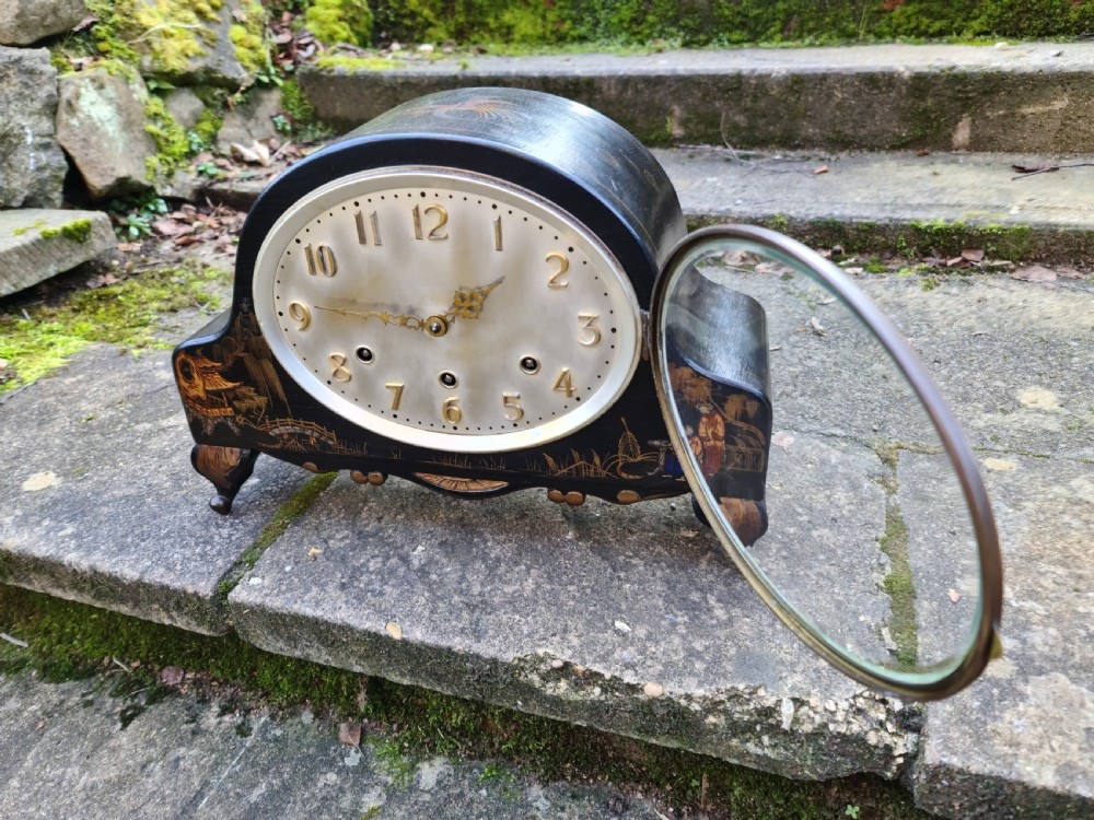 An antique black lacquered mantel clock decorated with gold chinoiserie scenes and an oval brass-rimmed clock face. View VI