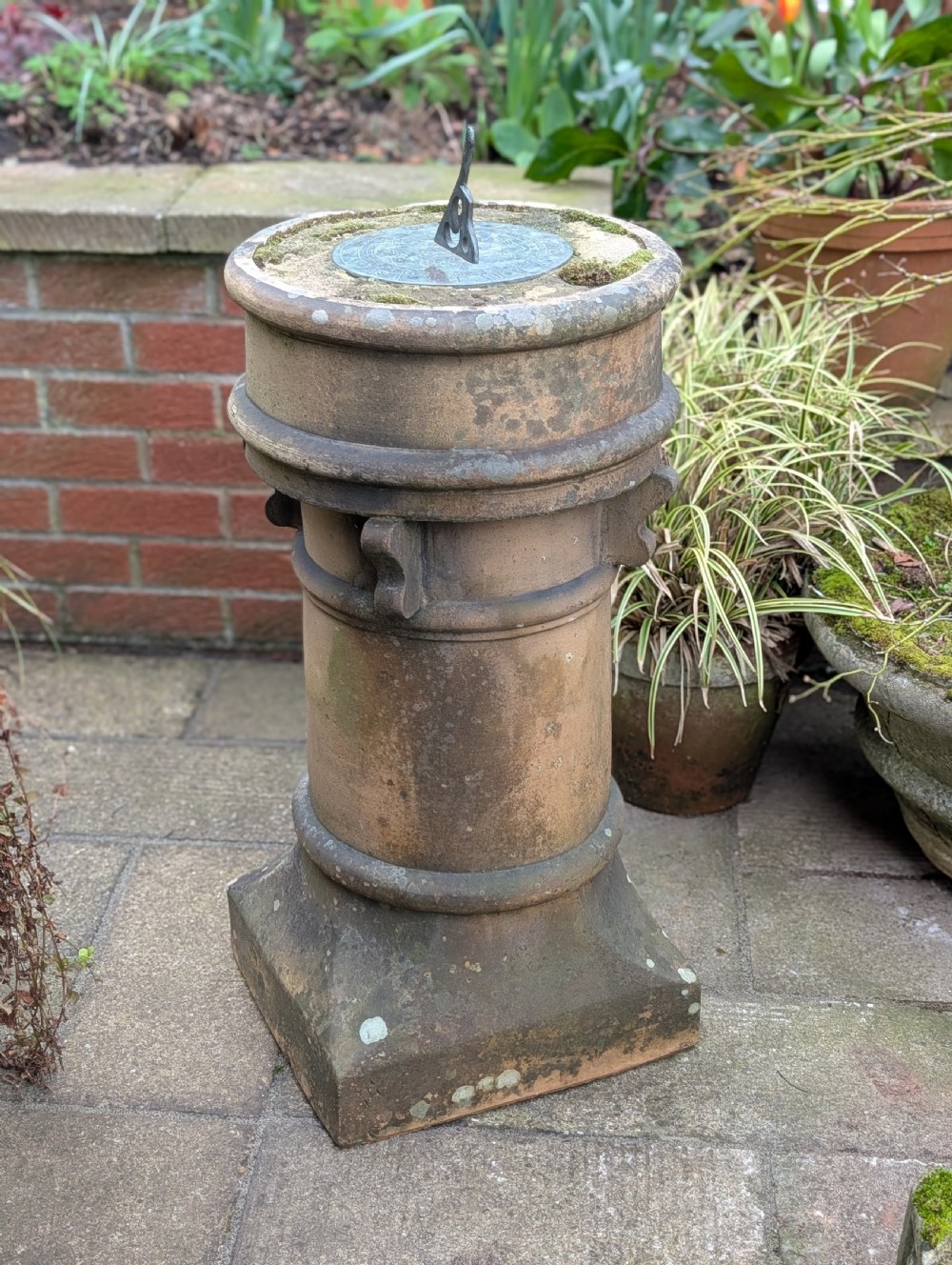 A nineteenth-century Victorian terracotta chimney pot repurposed as a garden sundial with a circular lead dial and gnomon.