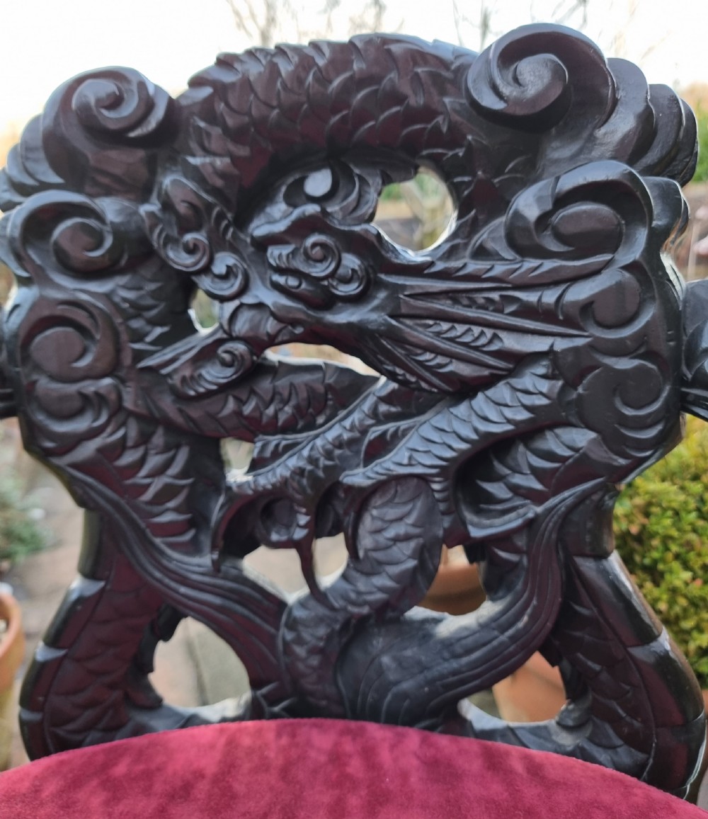 A dark carved hardwood armchair featuring carved dragon head armrests, an openwork backrest, cabriole legs, and a red velvet seat cushion. View V