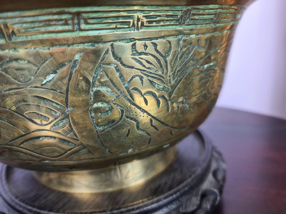 A large brass bowl featuring engraved dragon and cloud patterns with a flared rim, displayed on a dark carved wooden stand. View IV