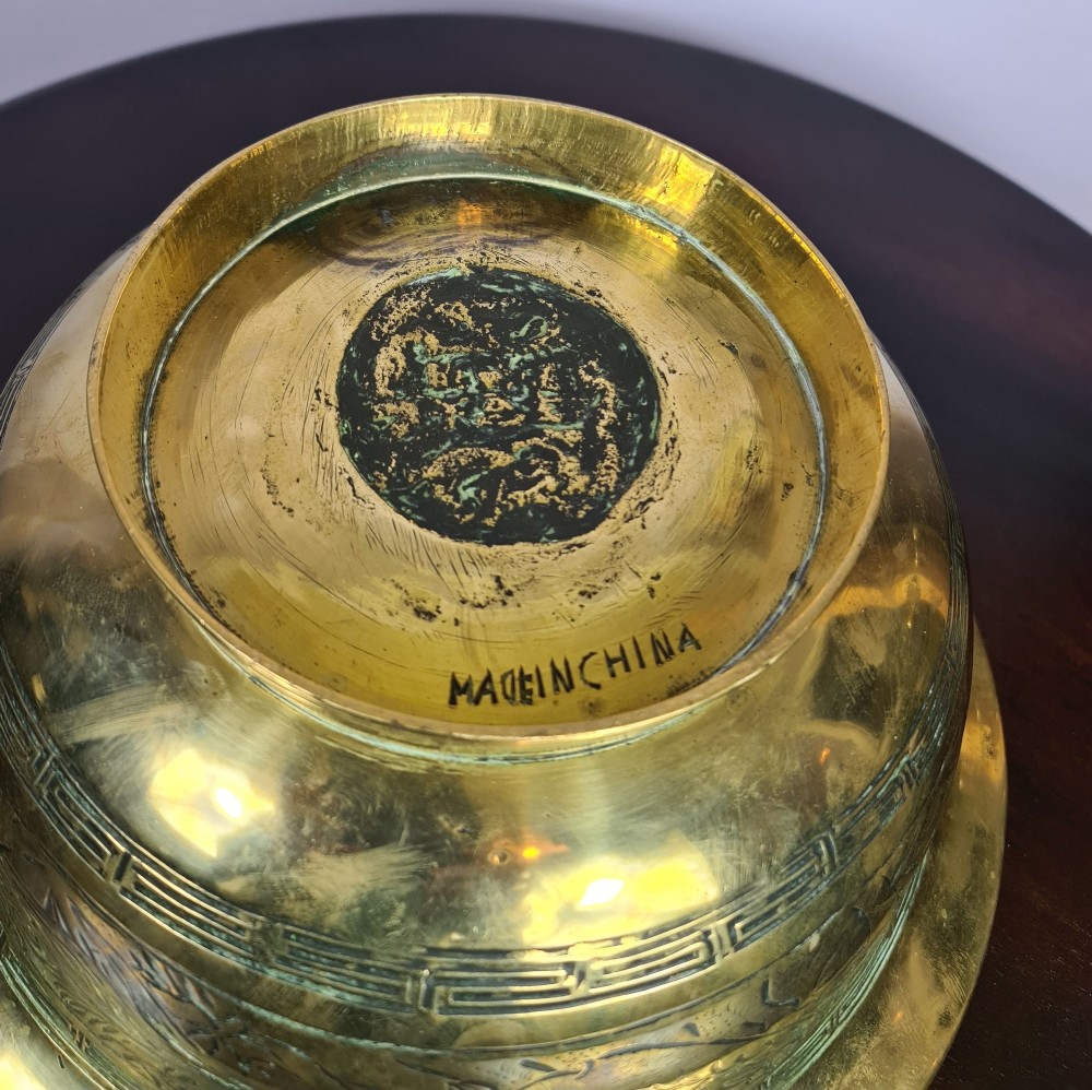 A large brass bowl featuring engraved dragon and cloud patterns with a flared rim, displayed on a dark carved wooden stand. View VI