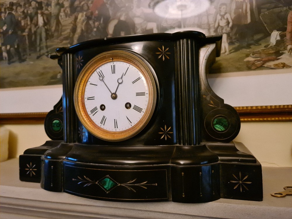 A Victorian black slate mantel clock featuring incised gilt star motifs, green malachite stone inlays, twin fluted columns, and a white enamel dial with Roman numerals.