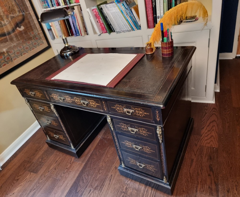 A dark ebonised Victorian pedestal desk featuring detailed floral marquetry inlay, brass handles, ormolu corner mounts, and a leather insert top. View VI