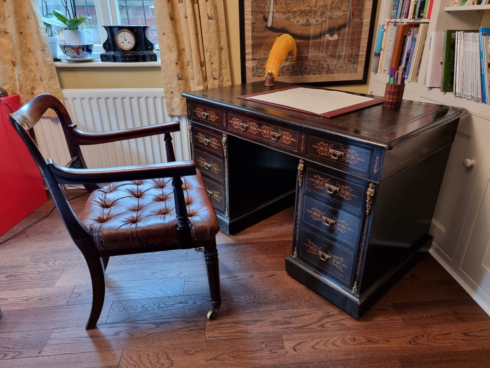 A dark ebonised Victorian pedestal desk featuring detailed floral marquetry inlay, brass handles, ormolu corner mounts, and a leather insert top. View X