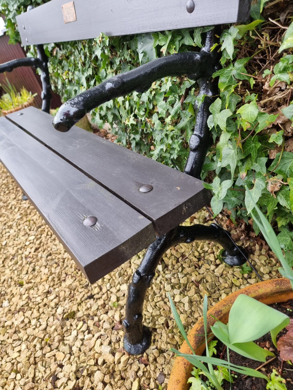 A 19th-century style garden bench featuring black cast-iron ends moulded into a branch motif with dark wooden slats forming the seat and backrest. View VI