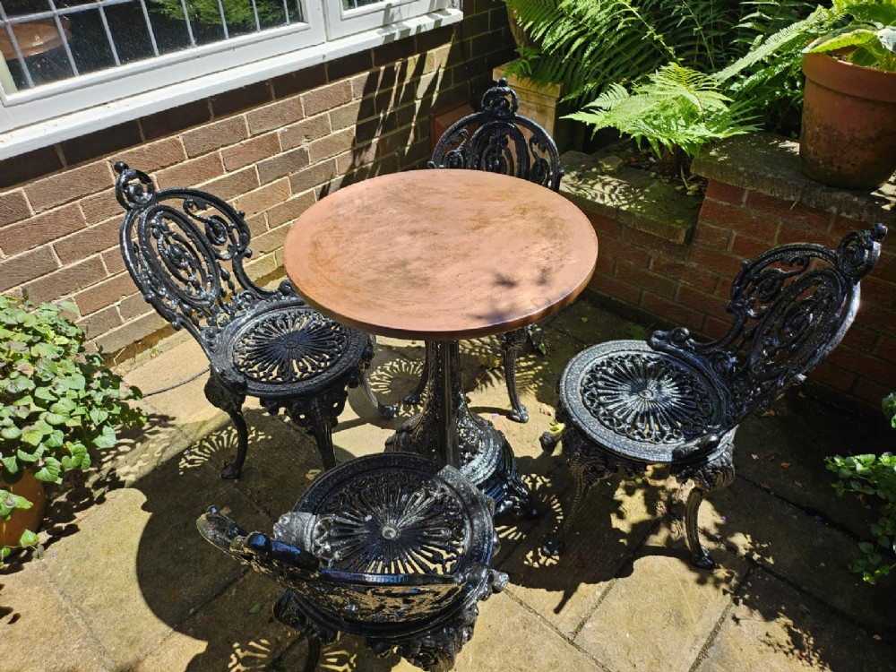 A Victorian cast iron garden set featuring a circular table with a copper top alongside four black ornate openwork chairs.