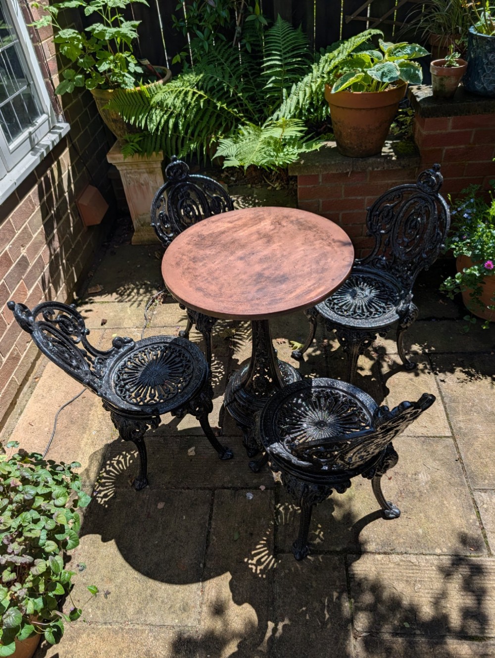 A Victorian cast iron garden set featuring a circular table with a copper top alongside four black ornate openwork chairs. View III