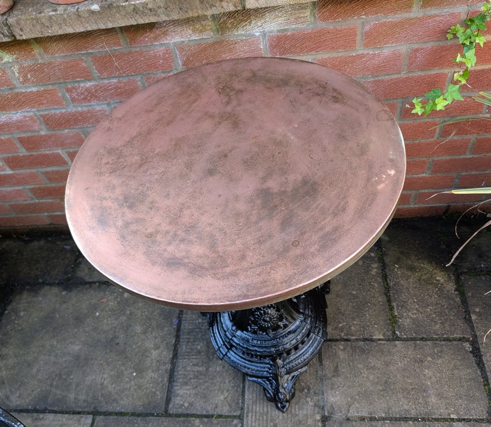 A Victorian cast iron garden set featuring a circular table with a copper top alongside four black ornate openwork chairs. View IX