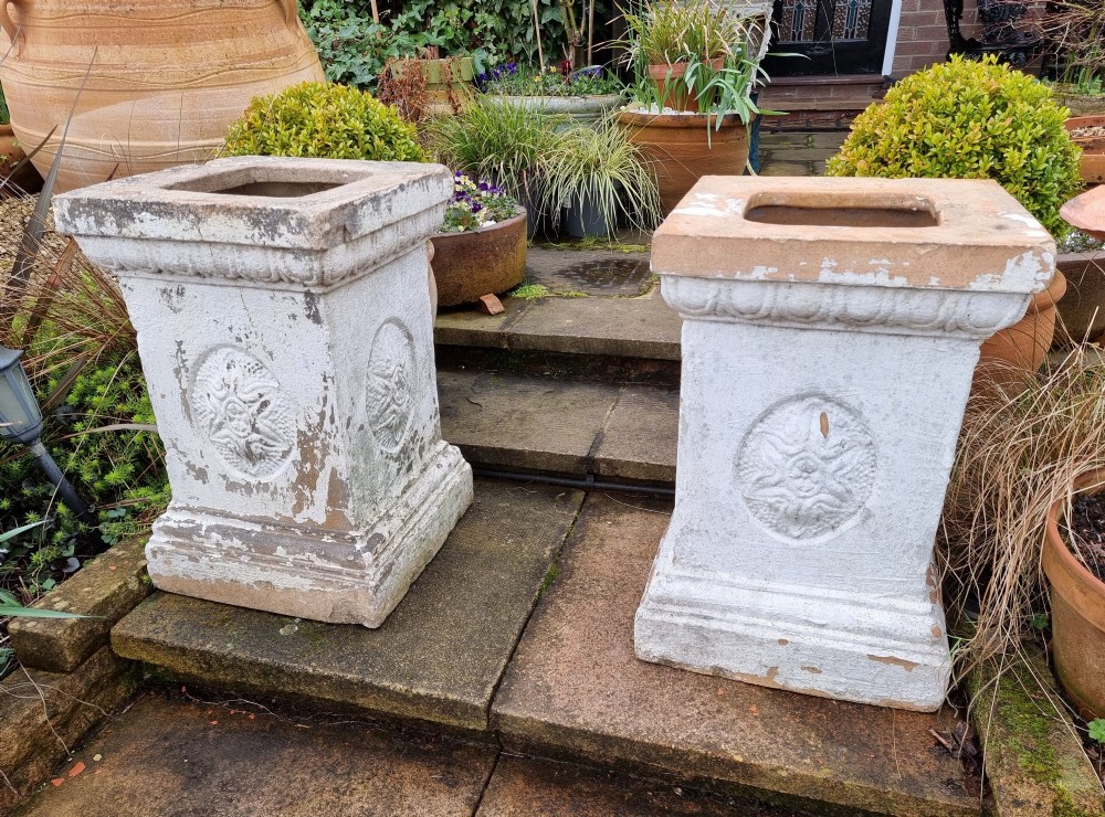 A pair of square weathered terracotta garden pedestals featuring moulded top rims and central circular floral medallion motifs.