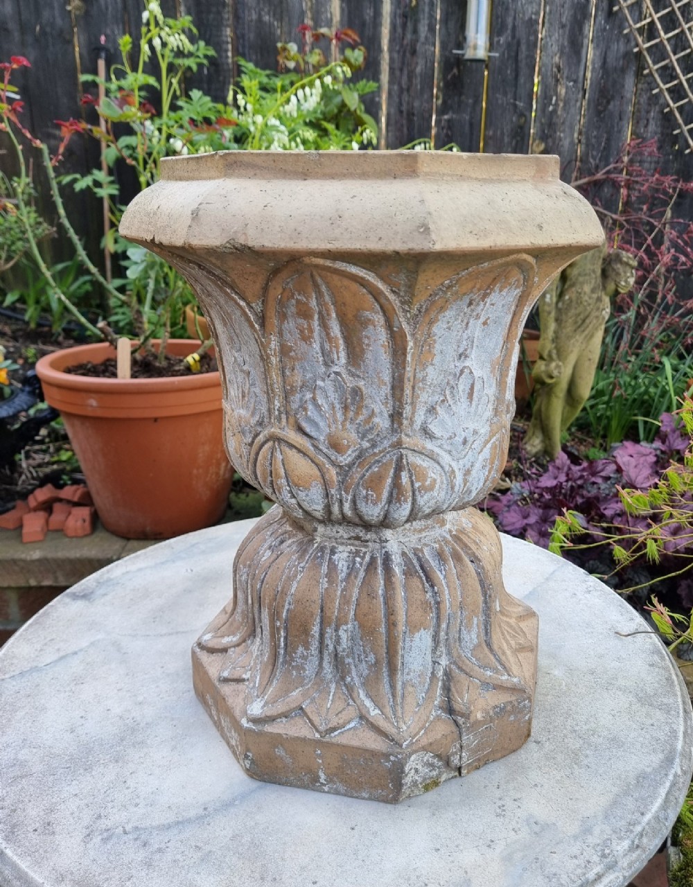 A 19th-century terracotta garden urn featuring carved leaf moulding, an octagonal top rim, and a flared pedestal base with weathered patina.