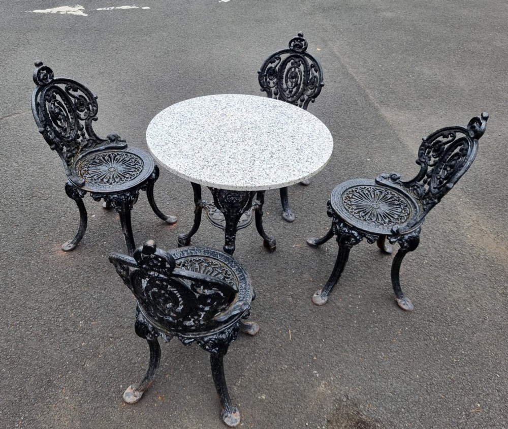 A black ornate cast-iron garden set featuring a circular stone-topped pedestal table and four matching pierced-back chairs.