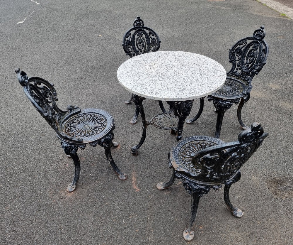A black ornate cast-iron garden set featuring a circular stone-topped pedestal table and four matching pierced-back chairs. View II