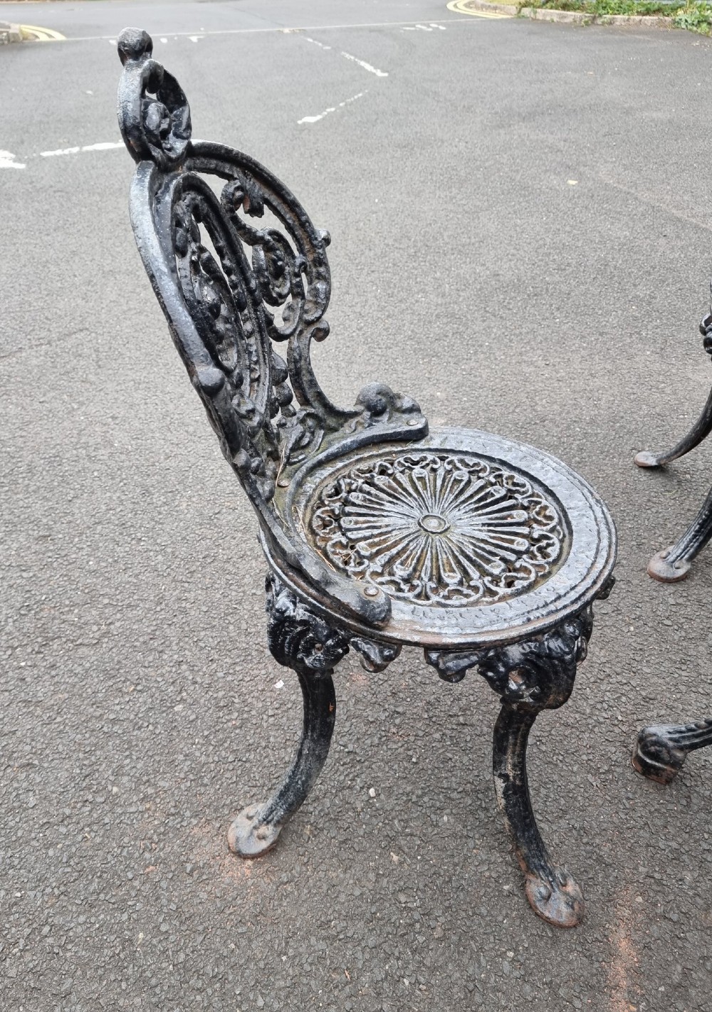A black ornate cast-iron garden set featuring a circular stone-topped pedestal table and four matching pierced-back chairs. View III