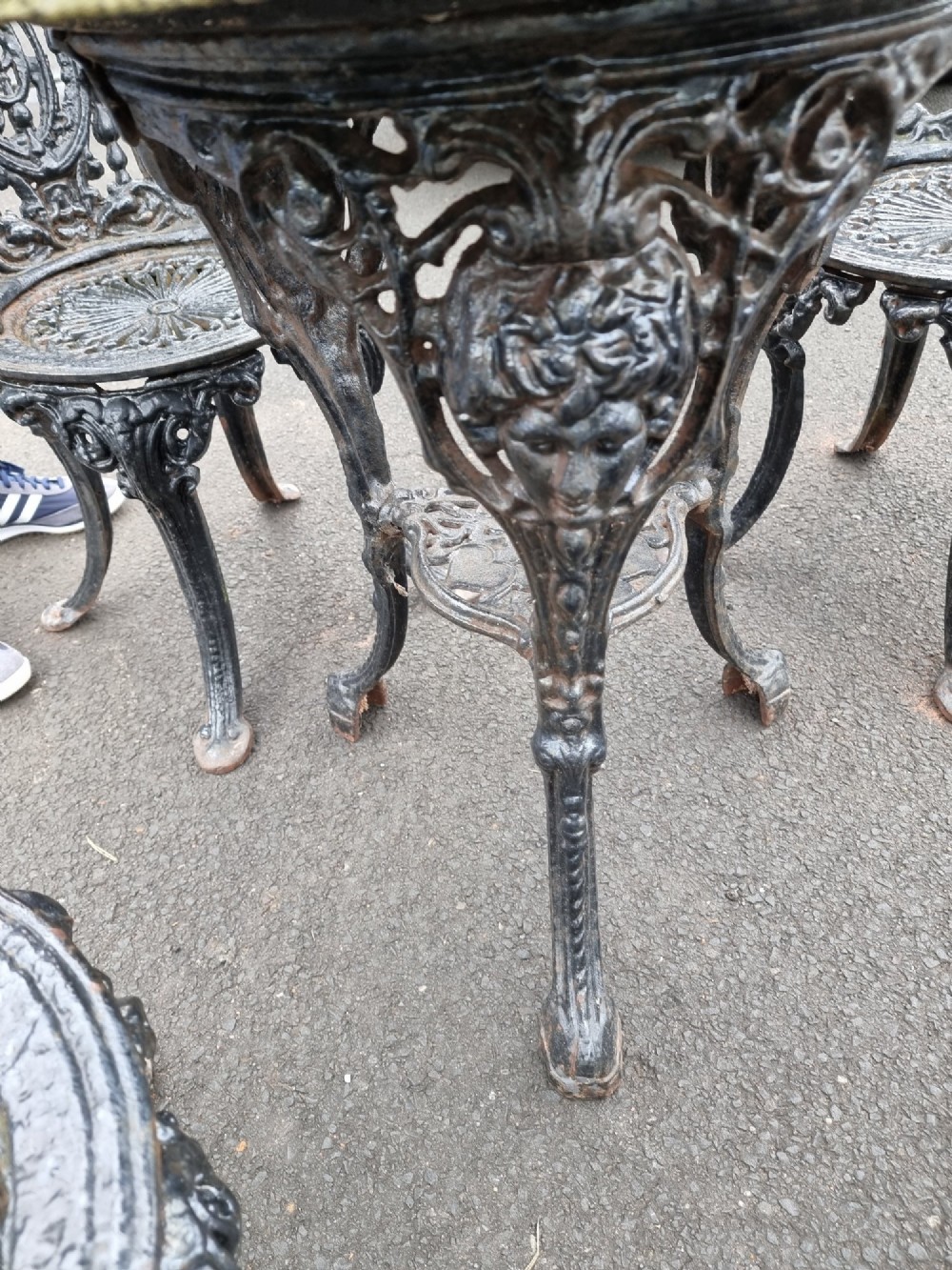 A black ornate cast-iron garden set featuring a circular stone-topped pedestal table and four matching pierced-back chairs. View IV