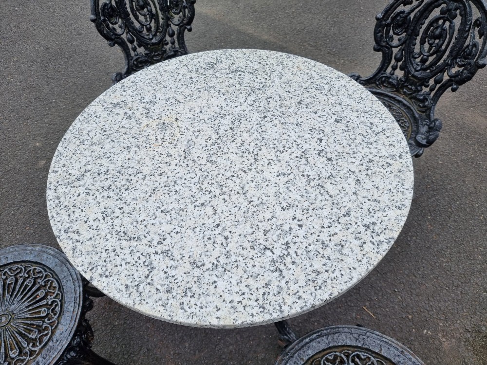 A black ornate cast-iron garden set featuring a circular stone-topped pedestal table and four matching pierced-back chairs. View VII