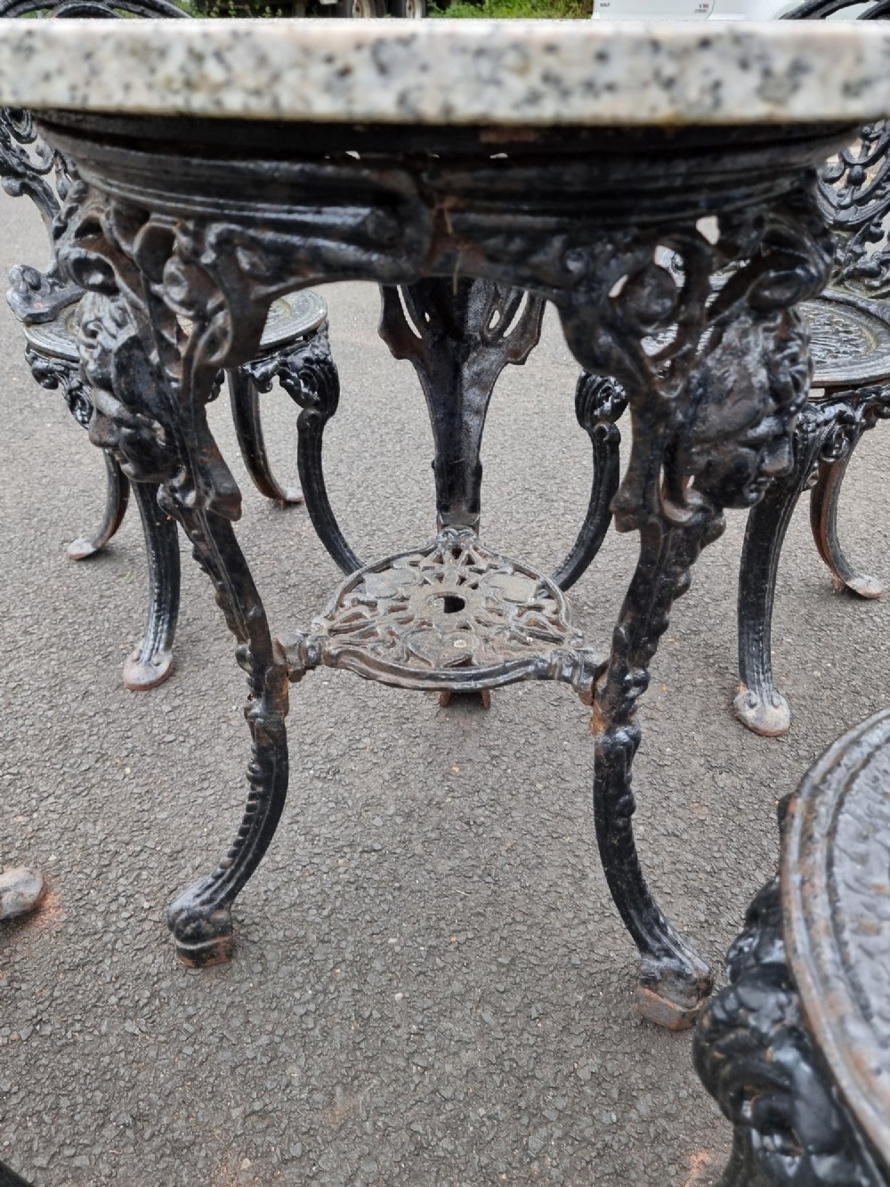 A black ornate cast-iron garden set featuring a circular stone-topped pedestal table and four matching pierced-back chairs. View VIII