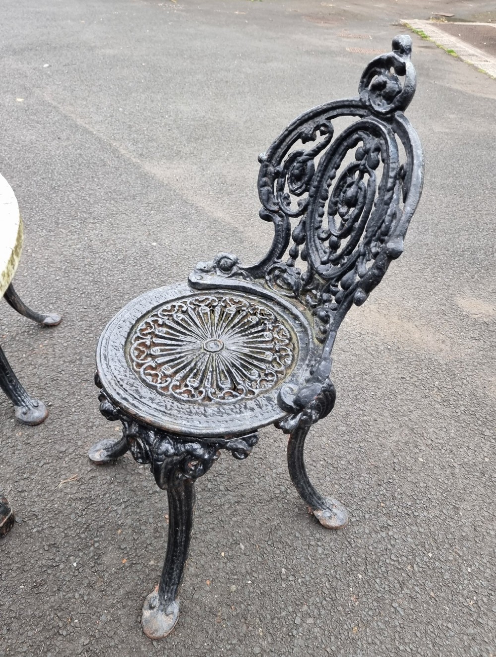 A black ornate cast-iron garden set featuring a circular stone-topped pedestal table and four matching pierced-back chairs. View XI
