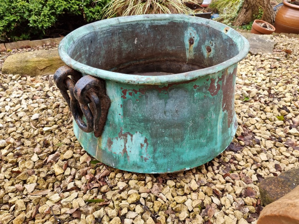 A large circular 19th-century copper vessel with a heavy verdigris green patina and dual wrought-iron drop handles.