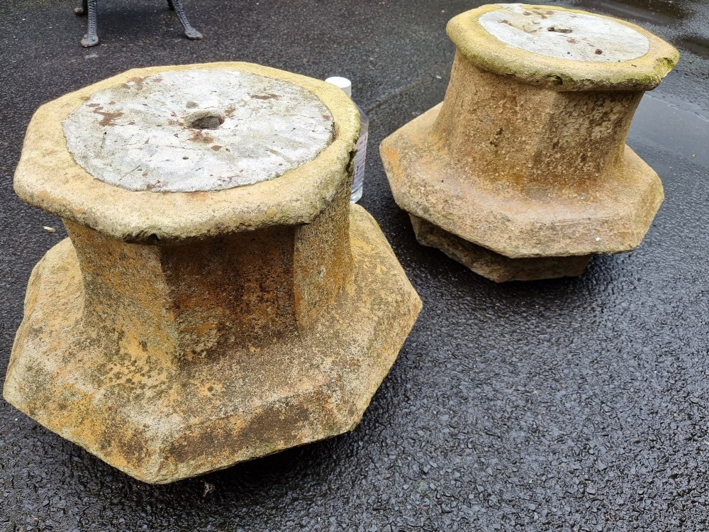 A pair of heavy octagonal composite stone garden plinths featuring moulded borders, central fixing holes, and weathered surface texture.