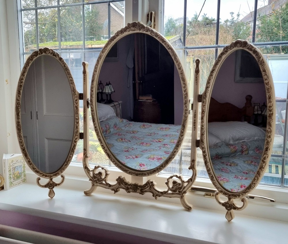 A 1930s cream-painted triple vanity mirror featuring three oval glass panels set in ornate scrollwork frames.
