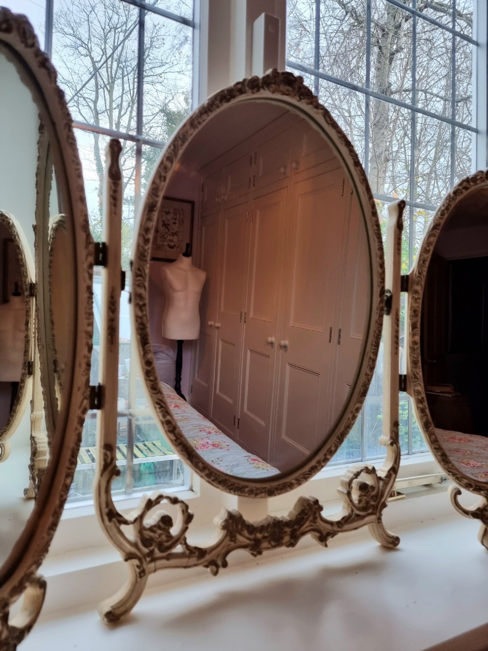 A 1930s cream-painted triple vanity mirror featuring three oval glass panels set in ornate scrollwork frames. View III