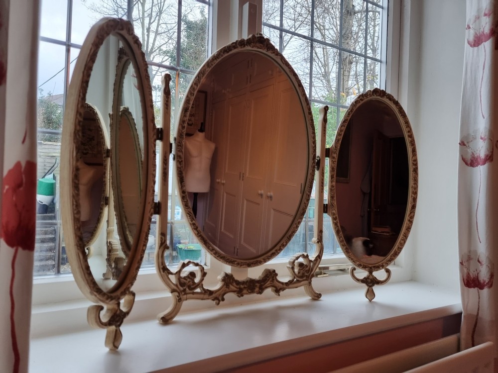 A 1930s cream-painted triple vanity mirror featuring three oval glass panels set in ornate scrollwork frames. View IV