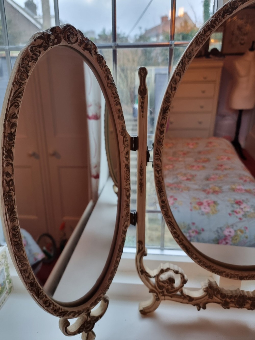 A 1930s cream-painted triple vanity mirror featuring three oval glass panels set in ornate scrollwork frames. View V