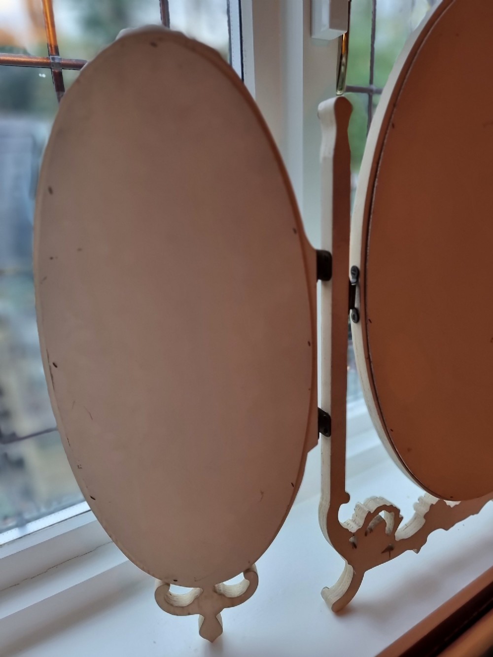 A 1930s cream-painted triple vanity mirror featuring three oval glass panels set in ornate scrollwork frames. View X