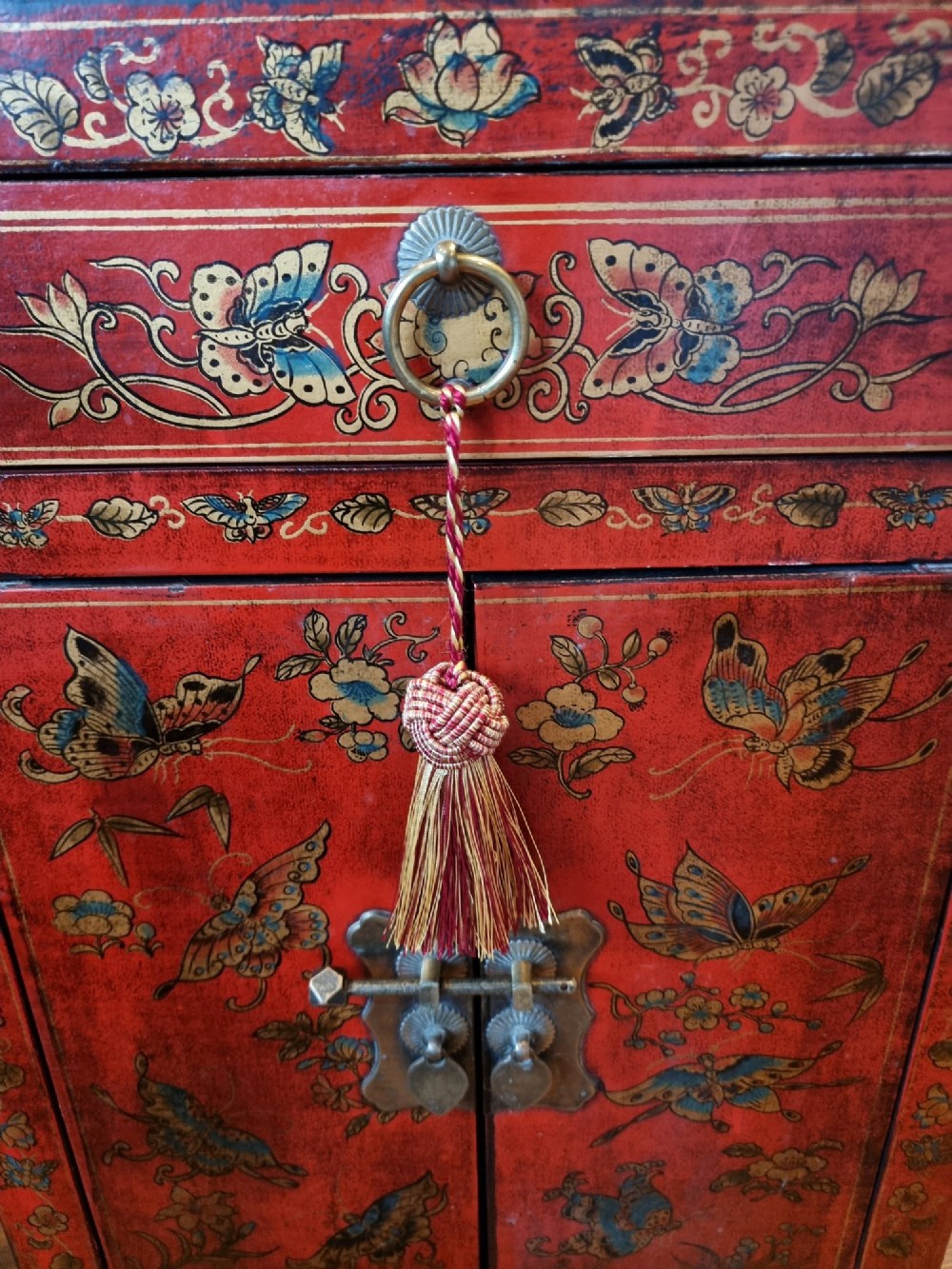 A small red and black hand-painted Chinoiserie cupboard featuring butterfly decoration, a single top drawer, two lower doors, and traditional brass hardware. View IV