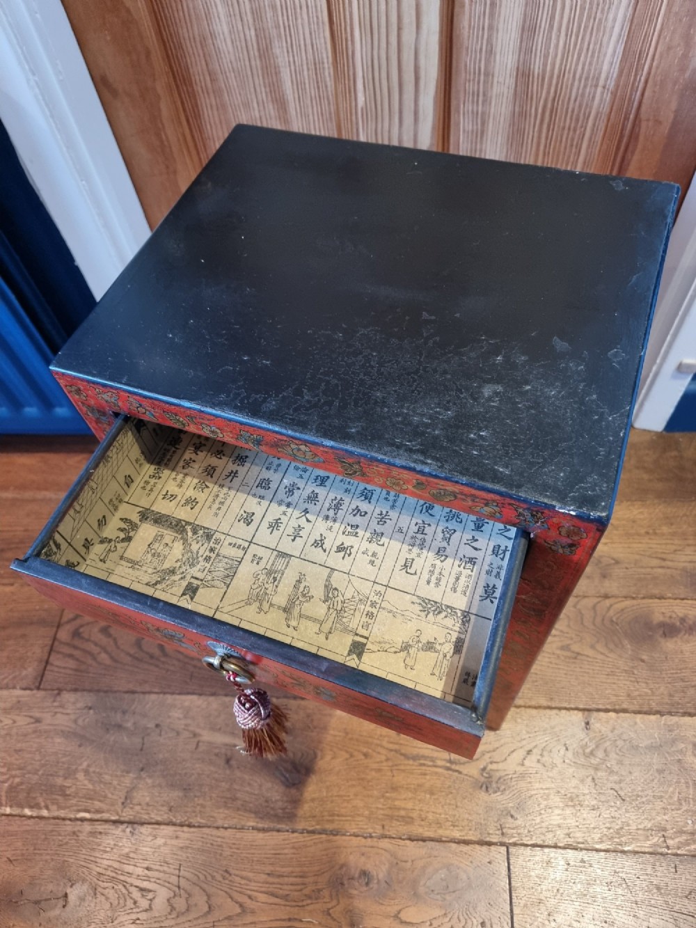 A small red and black hand-painted Chinoiserie cupboard featuring butterfly decoration, a single top drawer, two lower doors, and traditional brass hardware. View V