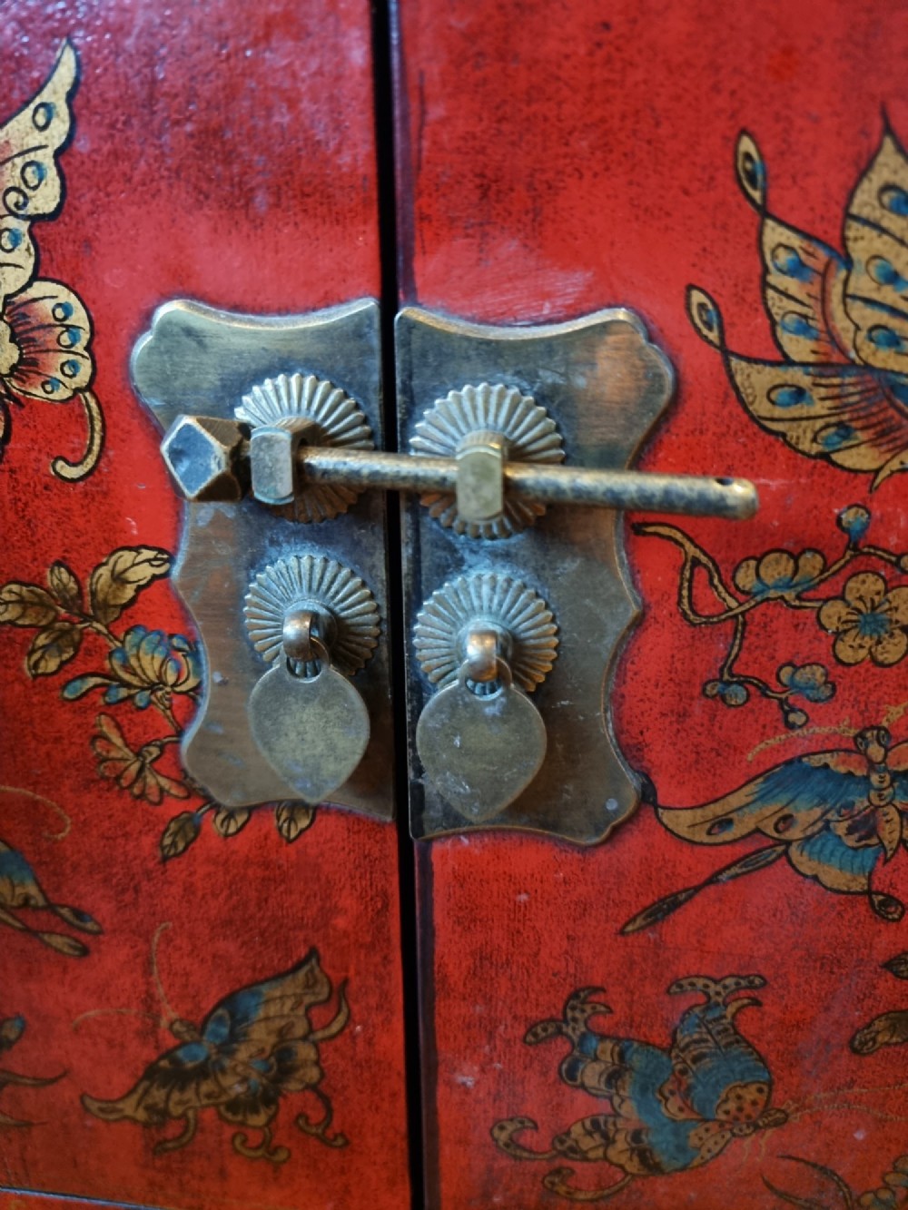 A small red and black hand-painted Chinoiserie cupboard featuring butterfly decoration, a single top drawer, two lower doors, and traditional brass hardware. View VI