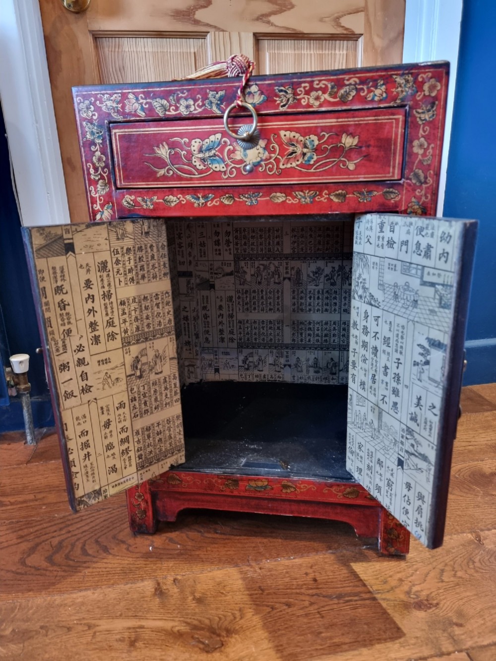 A small red and black hand-painted Chinoiserie cupboard featuring butterfly decoration, a single top drawer, two lower doors, and traditional brass hardware. View VII