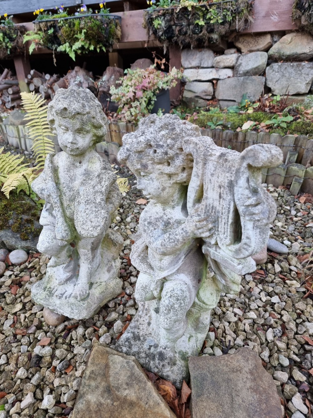 A pair of weathered grey reconstituted stone garden statues depicting classical musical cherubs holding instruments. View II