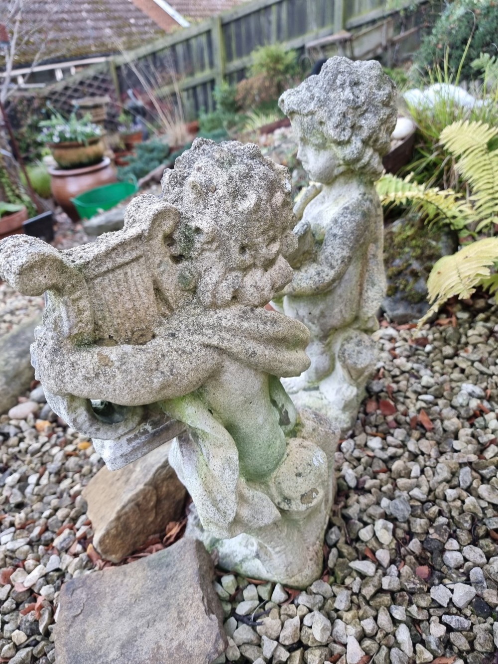 A pair of weathered grey reconstituted stone garden statues depicting classical musical cherubs holding instruments. View III