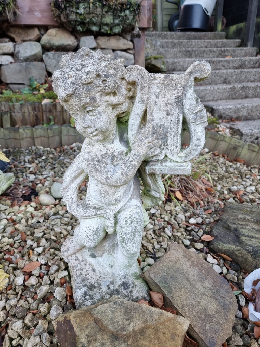 A pair of weathered grey reconstituted stone garden statues depicting classical musical cherubs holding instruments. View V