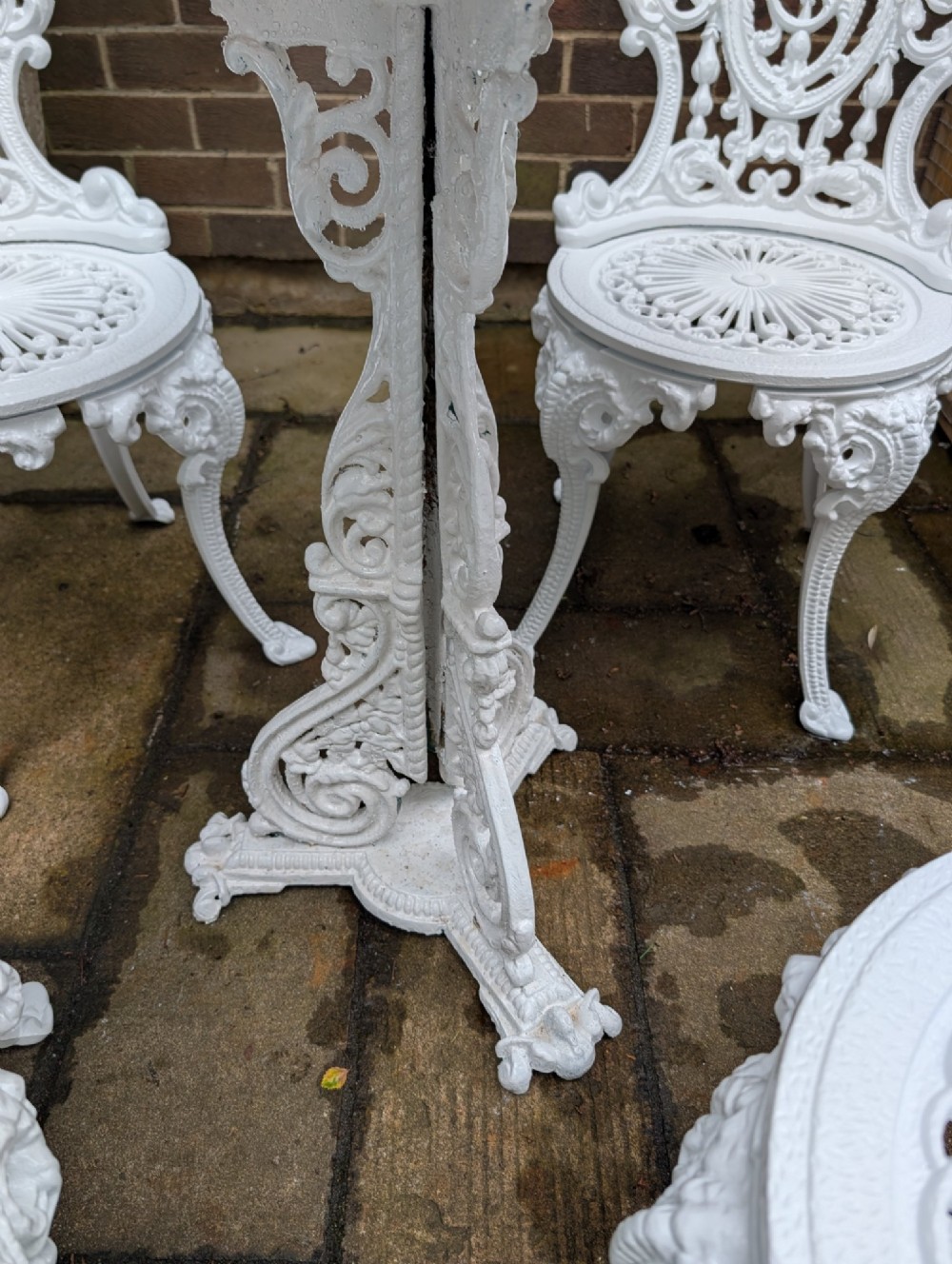 A white painted cast-iron garden set consisting of a round pedestal table and four ornate openwork chairs on a stone patio. View IV
