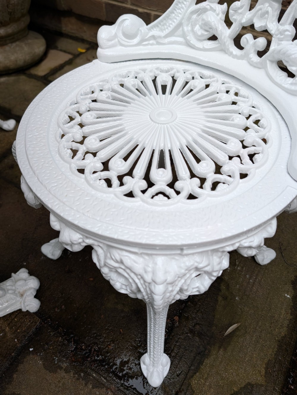 A white painted cast-iron garden set consisting of a round pedestal table and four ornate openwork chairs on a stone patio. View VII