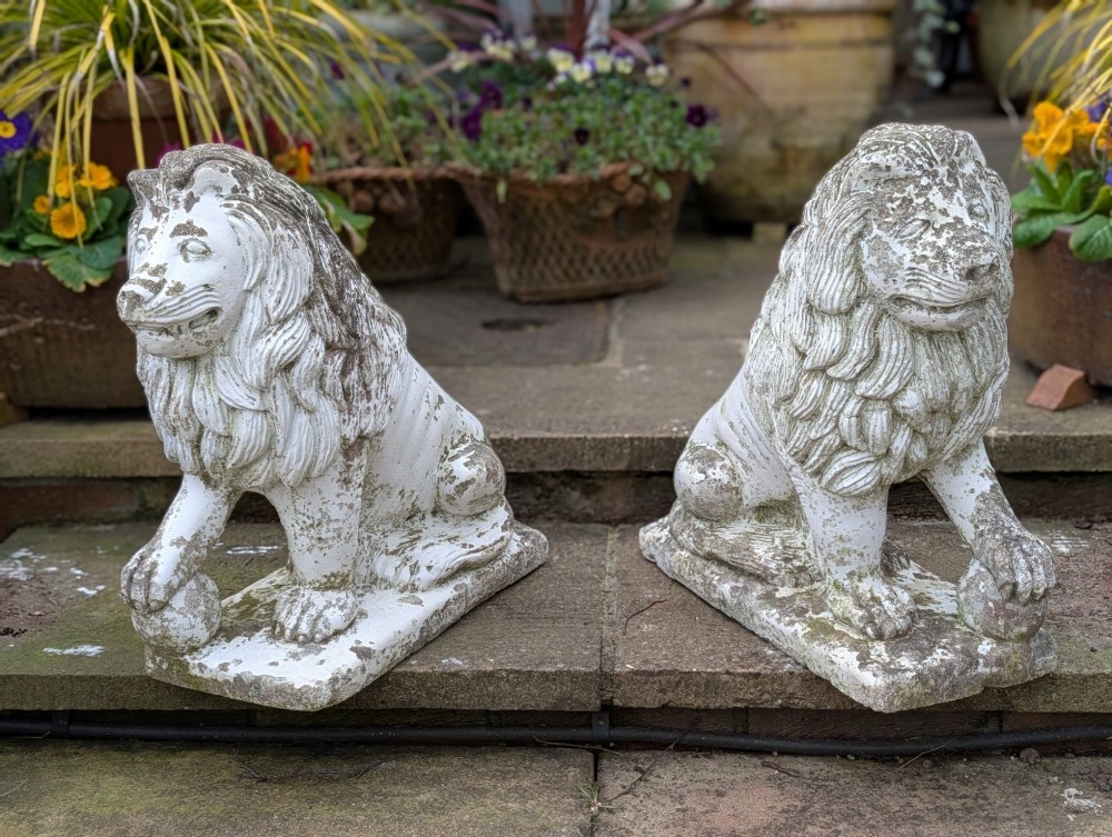 A pair of 19th-century French weathered off-white cast stone Medici lion statues seated on rectangular plinths, each resting a paw on a sphere.