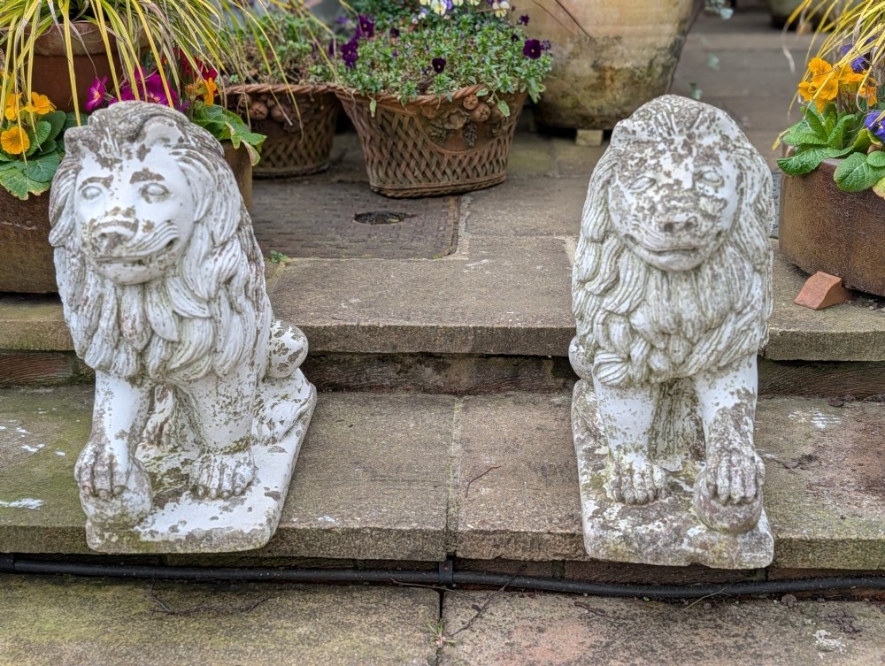 A pair of 19th-century French weathered off-white cast stone Medici lion statues seated on rectangular plinths, each resting a paw on a sphere. View II