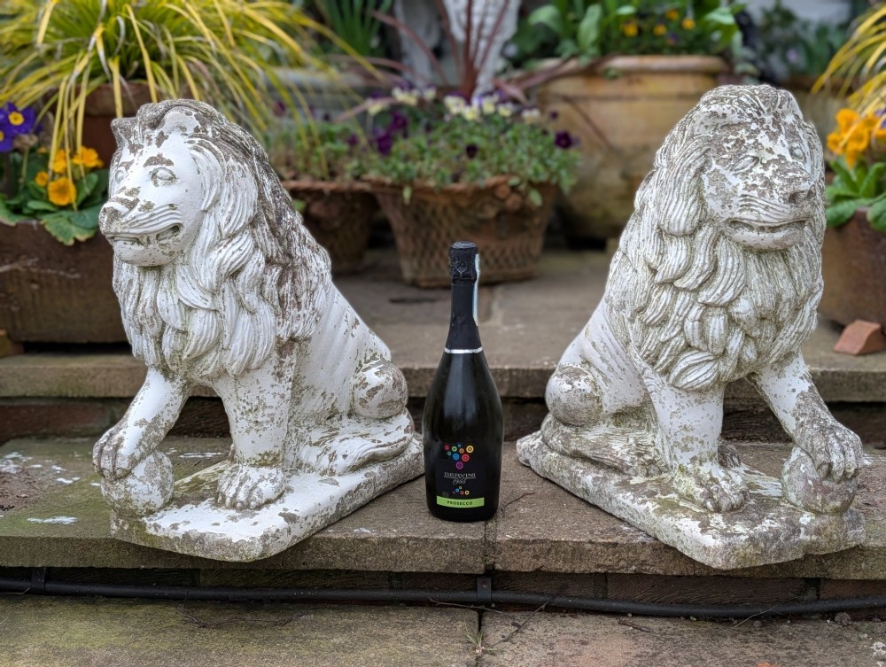 A pair of 19th-century French weathered off-white cast stone Medici lion statues seated on rectangular plinths, each resting a paw on a sphere. View VIII