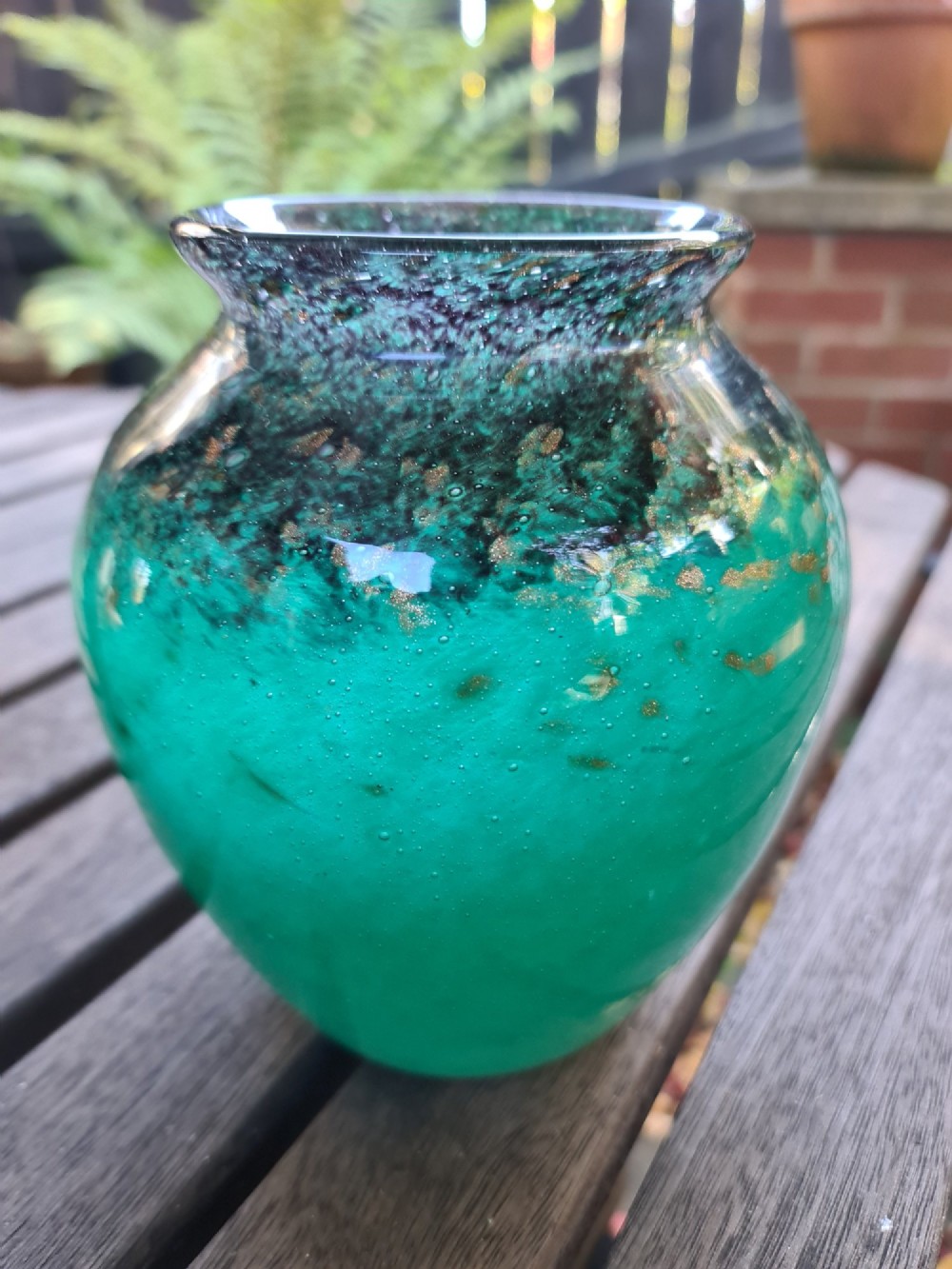 A rounded emerald green blown glass vase featuring a dark mottled rim, flared lip, and suspended gold aventurine flecks.