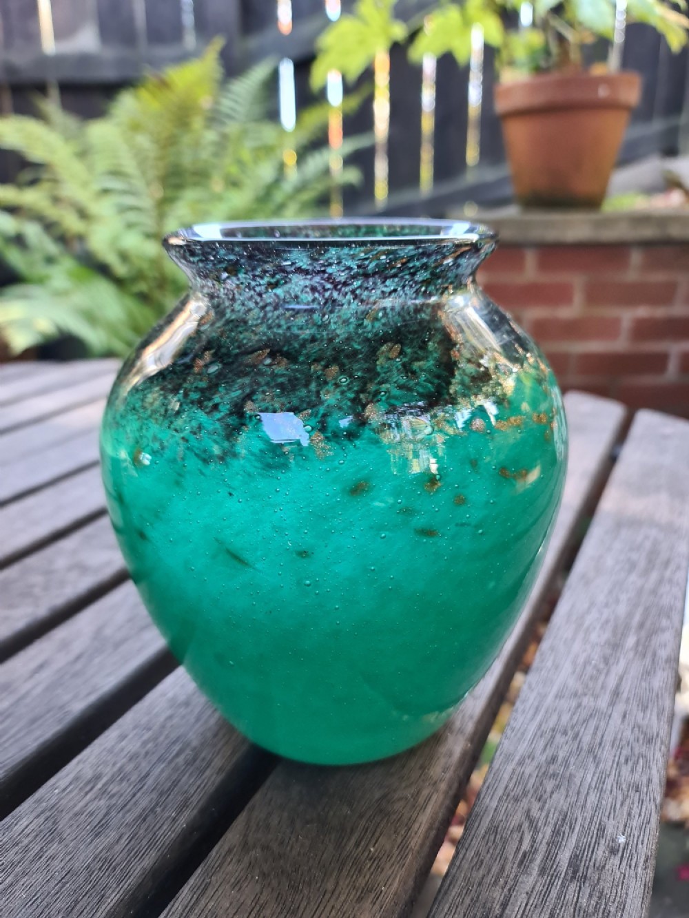 A rounded emerald green blown glass vase featuring a dark mottled rim, flared lip, and suspended gold aventurine flecks. View III