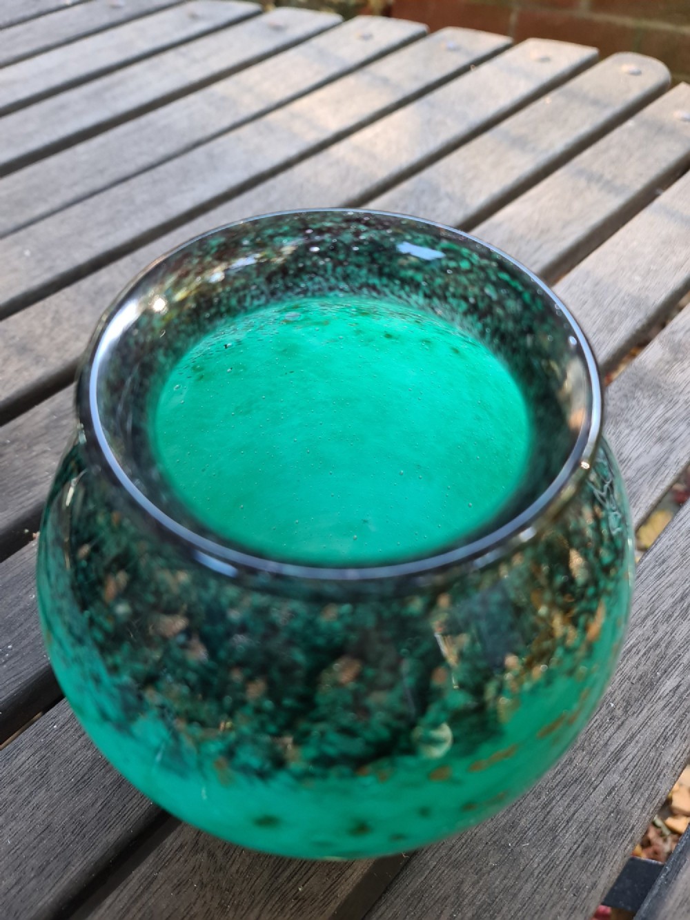 A rounded emerald green blown glass vase featuring a dark mottled rim, flared lip, and suspended gold aventurine flecks. View V