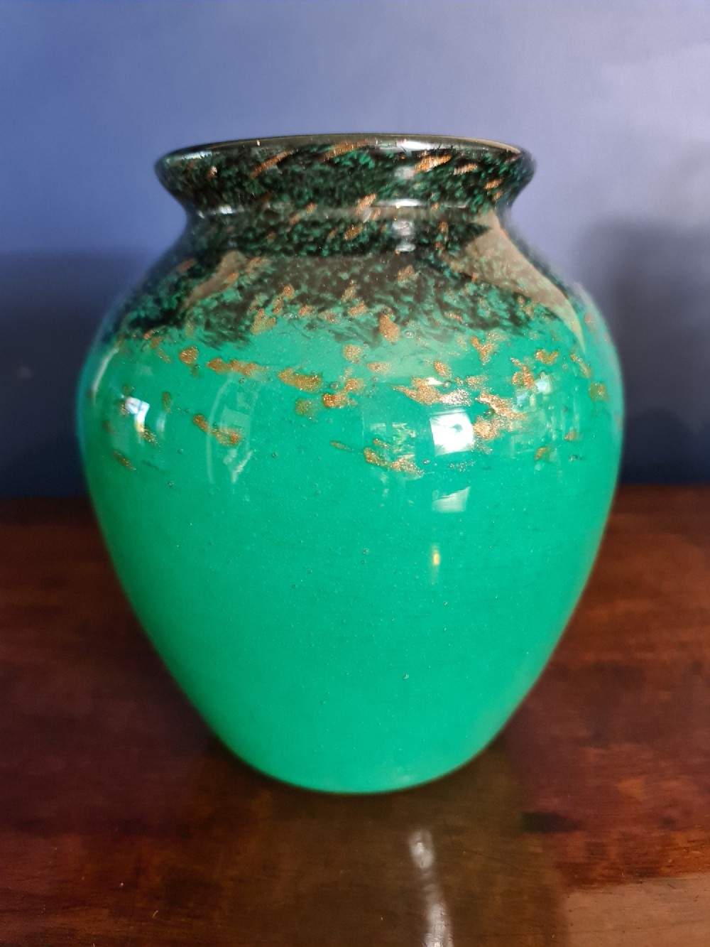 A rounded emerald green blown glass vase featuring a dark mottled rim, flared lip, and suspended gold aventurine flecks. View VII