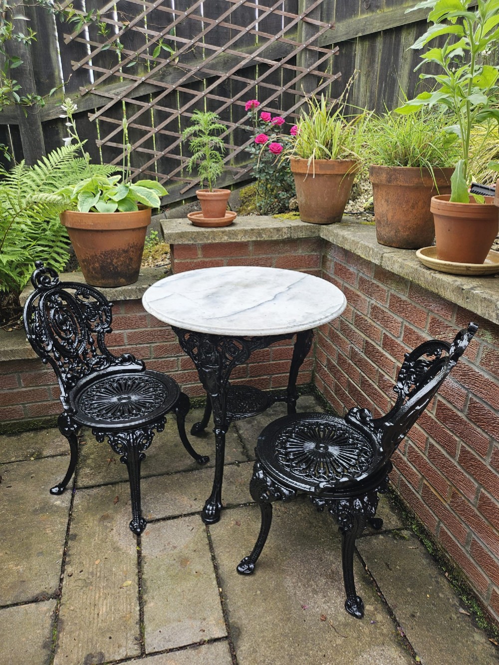A circular white marble-topped table with a black cast-iron base alongside two matching black cast-iron chairs featuring ornate pierced scrollwork. View II