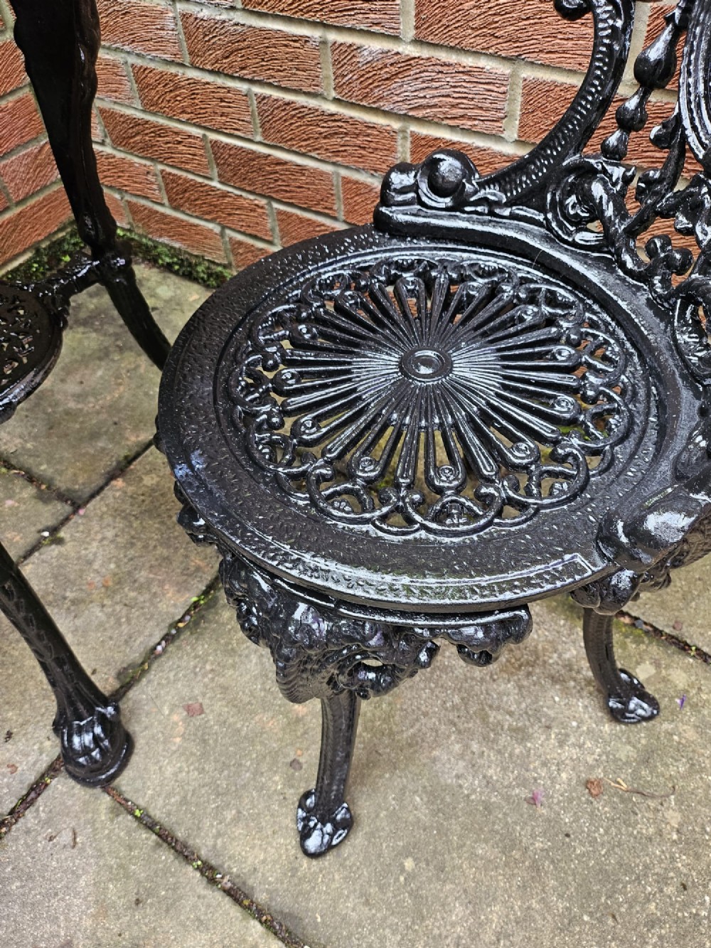 A circular white marble-topped table with a black cast-iron base alongside two matching black cast-iron chairs featuring ornate pierced scrollwork. View III