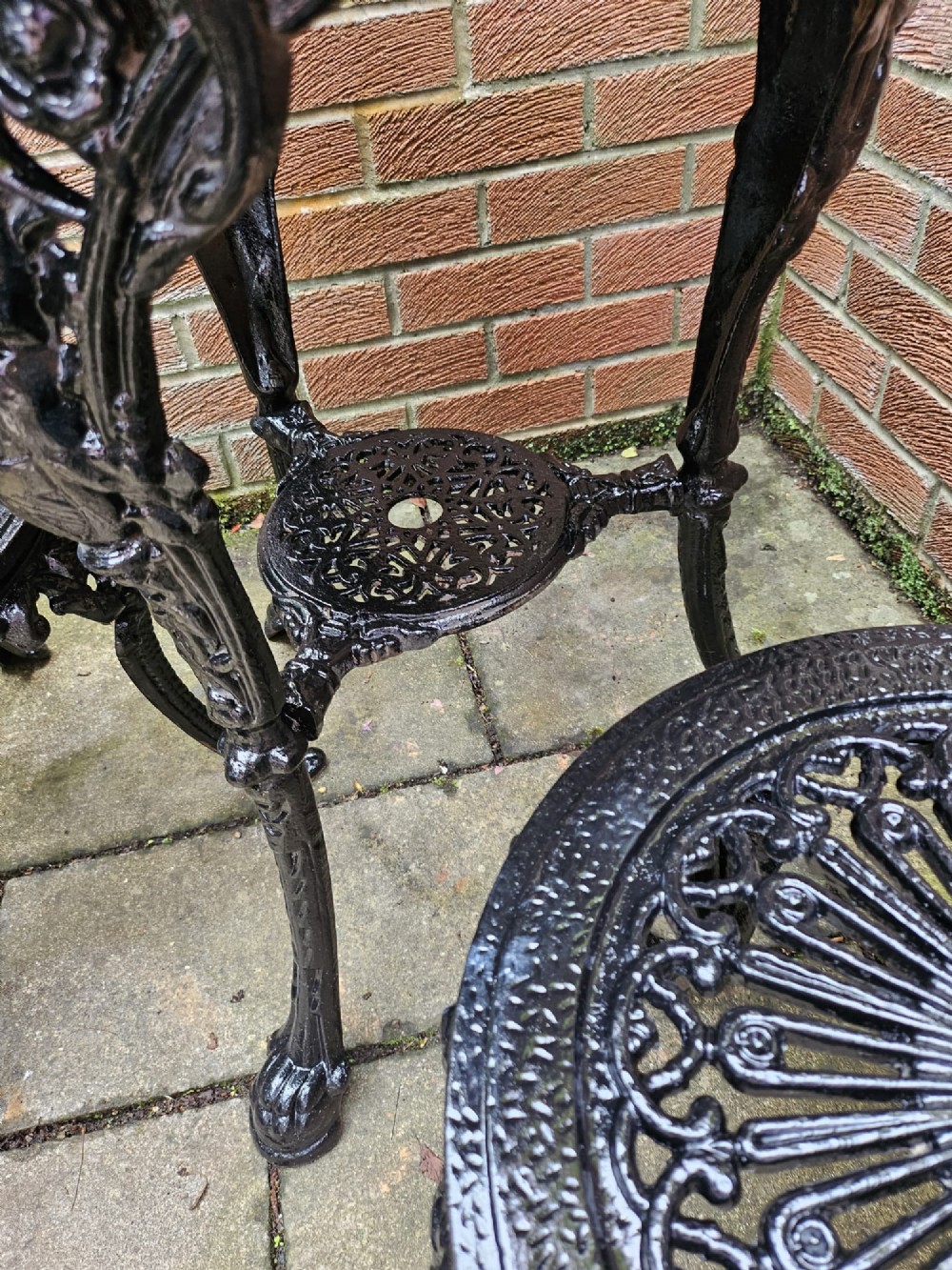 A circular white marble-topped table with a black cast-iron base alongside two matching black cast-iron chairs featuring ornate pierced scrollwork. View IV