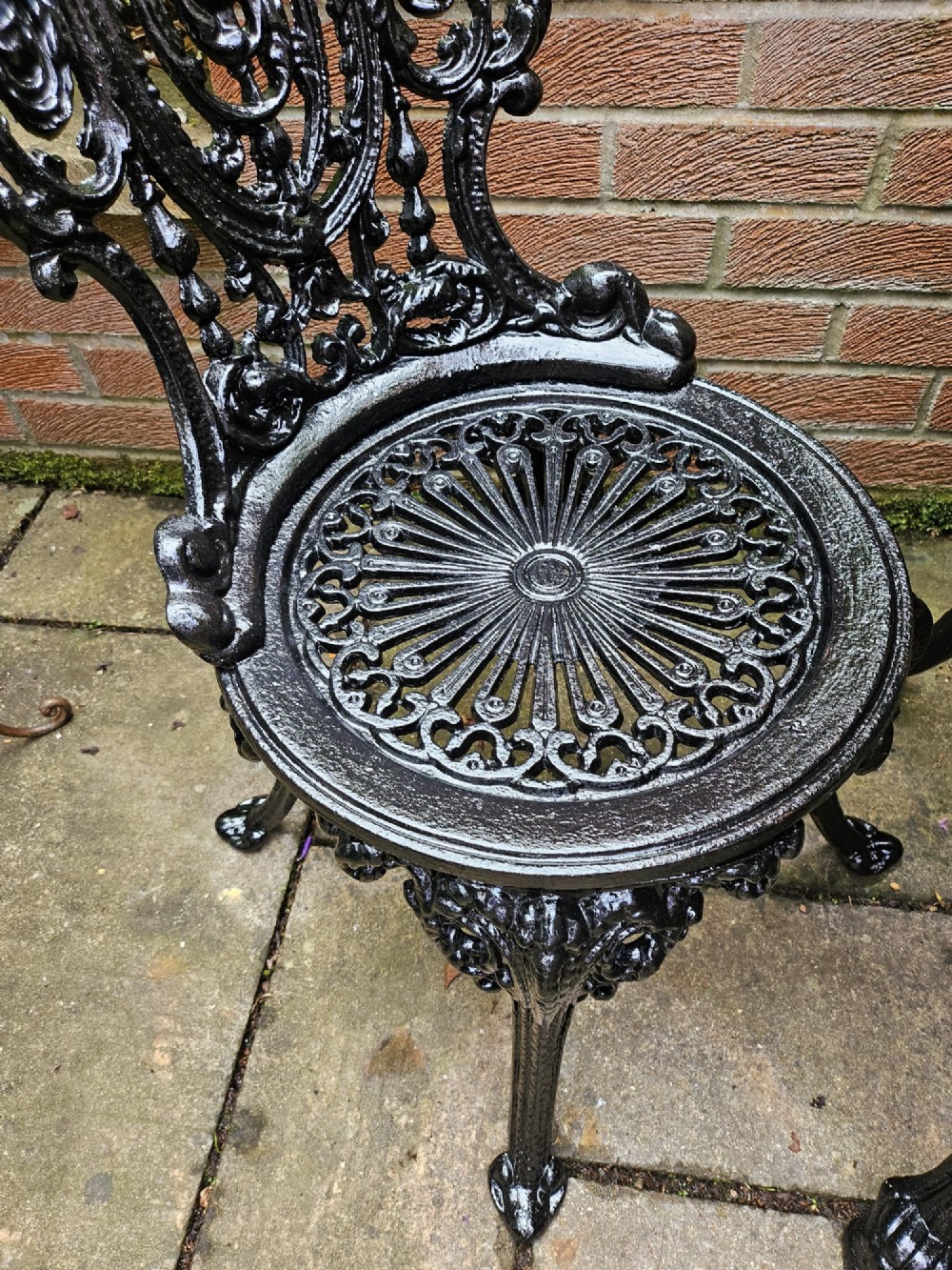 A circular white marble-topped table with a black cast-iron base alongside two matching black cast-iron chairs featuring ornate pierced scrollwork. View V